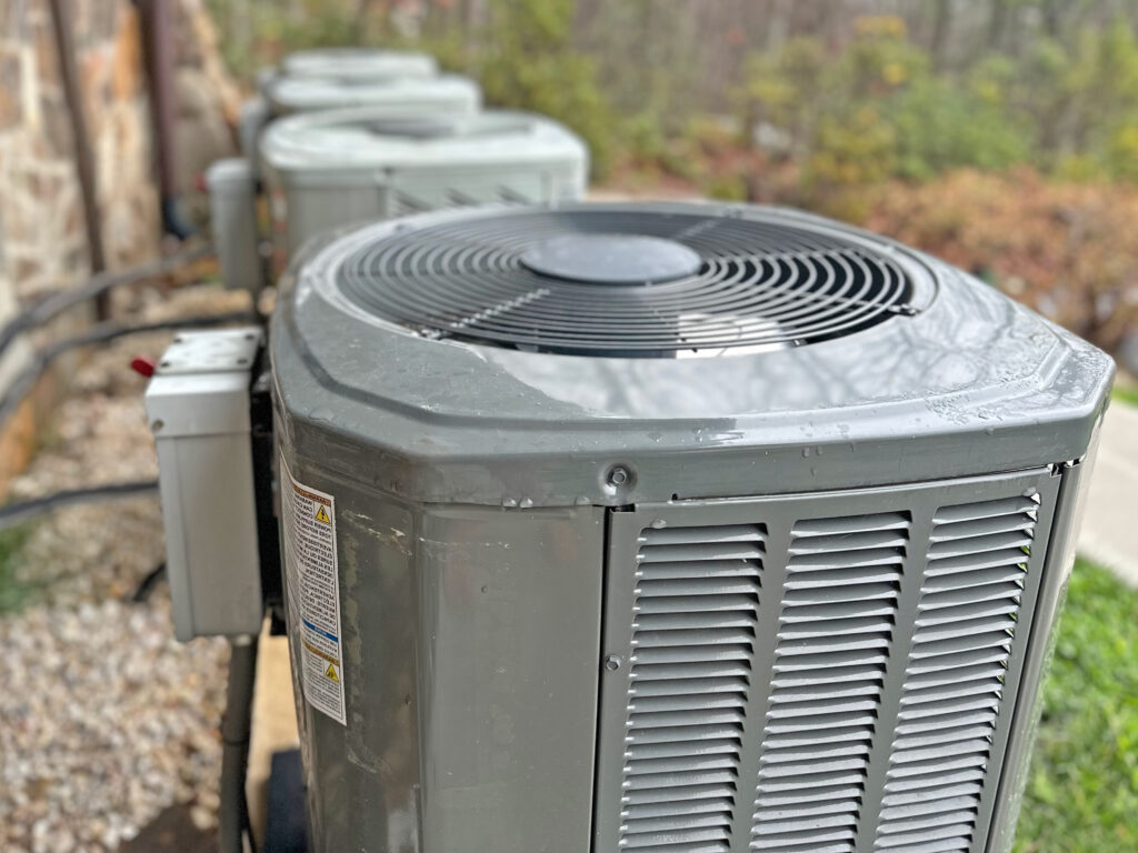 A row of outdoor air conditioning units, commonly part of energy-efficient HVAC cooling systems, placed beside a home, illustrating the importance of choosing Energy Efficient HVAC units