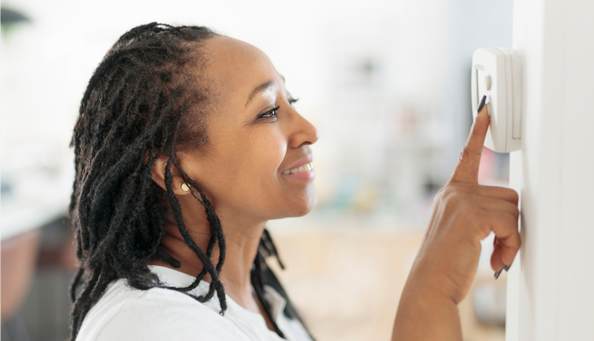 A smiling woman adjusts the thermostat to improve her heater's efficiency