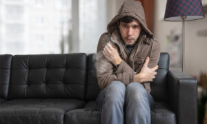 man wearing coat sitting on sofa shivering from cold